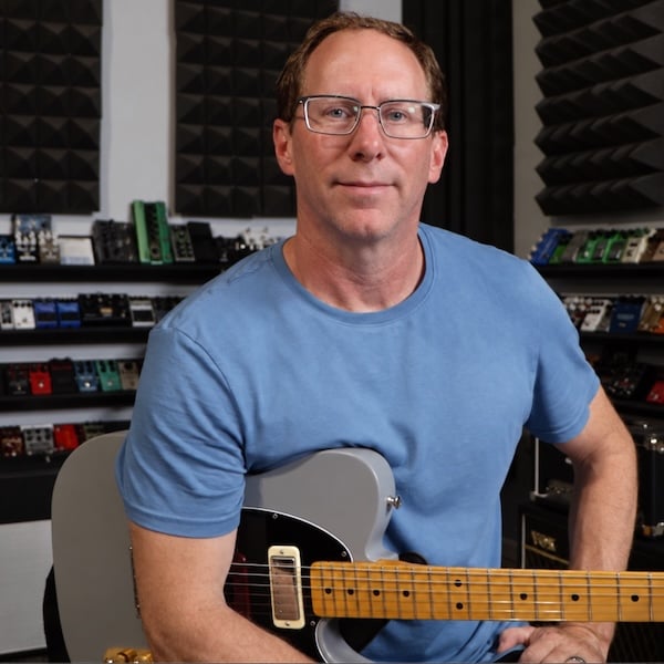 Brian Wampler, who built PedalSpice, holding a guitar in front of a wall of pedals